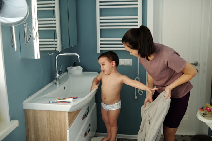 Anne, küçük oğluna lavaboda el yıkamayı gösteriyor